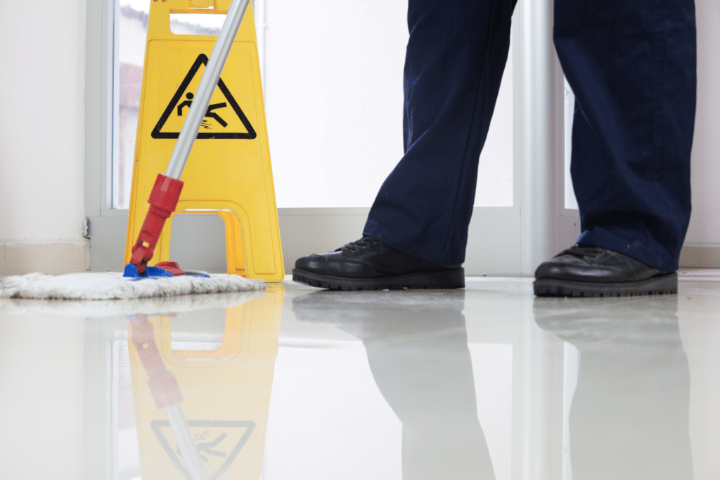 low angle closeup person cleaning floor with mop near yellow caution wet floor sign
